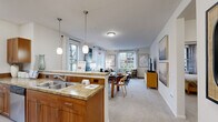 This single-floor, 3-bedroom, 1-bathroom residence offers a thoughtfully designed open-concept layout that seamlessly connects the kitchen, dining, and living areas. The kitchen features warm wood cabinetry, granite countertops, stainless steel appliances, and a peninsula with pendant lighting overhead, making it both functional and visually inviting. Light wood-tone flooring in the entryway transitions to plush carpeting throughout the main living spaces and bedrooms.

The combined dining and living area is bright and spacious, with multiple windows dressed in sheer white curtains that invite generous natural light and views of the surrounding greenery. A separate living room provides an additional gathering space with direct access to a covered outdoor patio, ideal for relaxing or entertaining.

The primary bedroom is generously sized, featuring carpeted floors, a large window, and ample room for furnishings. The two additional bedrooms offer comfortable proportions with natural light. The full bathroom is finished with granite countertops, wood cabinetry, a tub-shower combination, and wood-look flooring.

A welcoming entryway hallway with light flooring provides a clean transition into the home. A dedicated closet adds practical storage. The covered patio, accessible from the living room, extends the living space outdoors and offers a serene setting framed by mature trees.