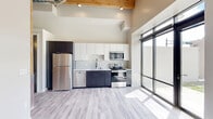 Located at 8 W 9th Ave in Oshkosh, Wisconsin, this single-floor unit offers a thoughtfully designed open layout with a striking blend of industrial and modern aesthetics. Soaring ceilings with exposed wooden beam rafters and a visible ductwork detail create a loft-like ambiance, adding significant vertical volume to the compact footprint.

The kitchen is a standout feature, outfitted with two-tone cabinetry — crisp white upper cabinets paired with dark lower cabinets — and a full suite of stainless steel appliances, including a refrigerator, dishwasher, over-the-range microwave, and electric range. Light-toned luxury vinyl plank flooring runs throughout, lending a clean and cohesive look to the space.

Natural light floods the interior through a dramatic floor-to-ceiling black-framed glass door and adjacent windows, offering direct views of the surrounding neighborhood. A secondary window further enhances the brightness of the open living area.

A sliding barn-style door leads to the closet, adding a charming rustic accent that complements the exposed wood ceiling above. The combination of high ceilings, abundant natural light, and carefully selected modern finishes makes this a well-appointed and visually distinctive space in the heart of Oshkosh.