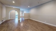 Located at 5407 Colfax Ave in North Hollywood, Los Angeles, this single-floor residence offers a well-organized layout comprising a living room, kitchen, and full bathroom. The living room is a generous, open space finished with warm wood-look flooring, neutral gray walls, recessed lighting, and a textured ceiling. A distinctive arched doorway serves as an architectural focal point, lending a classic touch to the otherwise modern interior. A pass-through window connects the living area to the kitchen, enhancing the sense of openness and flow between spaces. Natural light filters in through the windows, brightening the interior throughout the day. The galley-style kitchen is efficiently designed with white cabinetry, a tile floor, and a full suite of stainless steel appliances including a refrigerator, gas range, dishwasher, and microwave. A window above the counter provides additional natural light. The bathroom is clean and well-appointed, featuring a tiled tub and shower combo with frosted glass sliding doors, a white vanity with an undermount sink and stone-look countertop, and a window for natural ventilation. Overall, the space presents a cohesive, move-in-ready interior with modern finishes throughout.