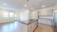 This single-floor residence offers a thoughtfully designed layout encompassing two bedrooms, two bathrooms, and two closets. The open-concept kitchen and living area serves as the heart of the home, centered around a large island with a dark granite countertop, undermount sink, and stylish pendant lighting overhead. White shaker-style cabinetry lines the kitchen walls, complemented by a classic subway tile backsplash and a full suite of stainless steel appliances, including a refrigerator, range, microwave, and dishwasher. Light wood-look flooring flows throughout the main living areas, enhancing the bright, airy feel created by recessed lighting and natural light from exterior-facing windows and a glass door. The primary bedroom features direct outdoor access through a glass door and multiple windows, while the second bedroom is finished with plush carpet and a ceiling fan, providing a comfortable retreat. Both bathrooms mirror the home's consistent design language, featuring granite-topped vanities with undermount sinks, white cabinetry, and wood-look flooring. One bathroom includes a full soaking tub and shower combination. Each bedroom is served by a dedicated closet with built-in shelving, maximizing storage throughout the space.