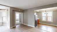 This well-organized single-floor residence offers two bedrooms, one bathroom, and a thoughtful layout connecting living, dining, and kitchen areas. The living room is a standout feature, highlighted by a graceful curved bay window that floods the space with natural light and adds architectural character. Light hardwood flooring runs throughout the main living and dining areas, complementing the neutral, textured wall finishes found throughout the home.

The kitchen is efficiently designed in an L-shaped configuration, featuring warm oak cabinetry, white countertops, tile flooring, and stainless steel appliances including a full-size refrigerator and dishwasher. A window above the sink provides natural light to the workspace.

Both bedrooms are carpeted and generously proportioned. The primary bedroom is notably spacious, offering built-in cabinetry with drawers, an open closet with integrated shelving, a ceiling fan, and multiple windows that bring in ample daylight. The second bedroom also includes a ceiling fan, a window, and access to additional storage.

The bathroom features classic white hex tile flooring and a distinctive arched walk-in shower alcove, lending a timeless, architectural touch. A connecting hallway ties all rooms together, creating a cohesive and functional flow throughout the residence.