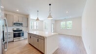 This two-story home offers a thoughtfully designed layout spread across two floors, combining modern aesthetics with practical functionality. The main floor hosts the open-concept kitchen and living area, finished with light hardwood-style flooring that enhances the bright, airy atmosphere created by multiple windows overlooking greenery. The kitchen is a standout feature, equipped with stainless steel appliances, light wood grain cabinetry with matte black hardware, quartz countertops, and a central island topped with two conical pendant lights. The living area flows seamlessly from the kitchen, offering generous space and direct exterior access.

Three full bathrooms serve the home, including one featuring a marble-tiled soaking tub and shower combination alongside a modern vanity with light wood cabinetry. A convenient half or full bath is also located on the main level. The upper floor accommodates both bedrooms, including a spacious primary suite with a ceiling fan, plush carpeting, a walk-in closet outfitted with wire shelving, and a private en-suite bathroom. The secondary bedroom is also carpeted and well-proportioned. A hallway and two staircases complete the upper level's layout, ensuring smooth circulation throughout the home.
