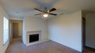 Located in Lewisville, TX, this single-story space offers a comfortable and functional layout with a warm, understated aesthetic. The living area serves as the centerpiece of the home, highlighted by a classic white brick fireplace that adds a traditional focal point and a sense of coziness to the room. A five-blade ceiling fan with a built-in light fixture is centrally mounted on the textured ceiling, providing both air circulation and ambient lighting. The room is finished with wall-to-wall carpeting in a neutral tone, contributing to a soft and inviting atmosphere. The walls are painted in a light, neutral hue, creating a clean and versatile backdrop that suits a variety of décor styles. A doorway visible along one side of the living area suggests a connected layout, allowing for easy flow between spaces. The overall design is straightforward and practical, with finishes that offer a solid foundation for personalization. The space presents a relaxed, livable environment well-suited for everyday comfort in a suburban Lewisville setting.