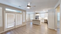 Located at 3880 FM 2920 in Spring, TX, this single-story 2-bedroom, 2-bathroom home offers a thoughtfully designed open-concept layout. The living room features light wood-look flooring, a ceiling fan, and a set of French doors flanked by windows that allow abundant natural light to fill the space. The kitchen is a standout, showcasing white shaker-style cabinetry extending to the ceiling, a classic subway tile backsplash, granite countertops, a large central island, and a full suite of stainless steel appliances including a refrigerator with ice maker, range, microwave, and dishwasher. Recessed lighting adds a polished touch overhead. Both bedrooms are carpeted, each equipped with a ceiling fan and window with blinds, providing a comfortable and quiet retreat. The hallways connect to two closets, offering practical storage solutions. The bathrooms are finished with granite-topped vanities, wood-look flooring, and brushed nickel fixtures; one includes a tub-shower combination with tile surround. Neutral warm-toned walls throughout create a cohesive and move-in-ready ambiance suited for a variety of lifestyles.