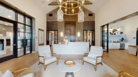 This single-floor amenity space masterfully blends contemporary design with rustic, industrial elements to create an inviting and multifunctional environment. The reception area immediately establishes the aesthetic tone, showcasing dramatic vaulted ceilings with exposed wooden beams, a striking reclaimed wood and oxidized metal accent wall, and a statement circular brass chandelier with woven pendant lights. Light-toned hardwood flooring runs throughout, unifying the various zones seamlessly.

The welcoming lounge area near the entrance features white upholstered armchairs with warm wood frames arranged around a marble-top side table, bathed in abundant natural light pouring through floor-to-ceiling windows. Black-framed steel-and-glass partition doors lend an industrial sophistication that recurs throughout the space.

A dedicated entertainment and games area showcases exposed whitewashed brick columns, a foosball table, shuffleboard, a wall-mounted television, and a bar counter with stylish globe pendant lighting. Adjacent to this, a well-appointed kitchenette with white cabinetry, bar seating, and pendant lighting serves as a practical gathering hub.

A separate lounge zone features soaring ceilings, large windows that flood the room with daylight, curated artwork, and elegant furnishings. A dining area with a solid wood table, slipcovered chairs, and nearby wet bar completes this versatile, thoughtfully designed communal space.