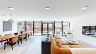 Located at 1314 Spring Garden St in Philadelphia, PA, this single-floor space offers a thoughtfully designed layout that blends modern aesthetics with functional versatility. The combined dining and living area serves as the heart of the space, characterized by clean white walls, large floor-to-ceiling sliding glass doors, and oversized spherical pendant lighting that creates a warm, inviting atmosphere. The dining area features a substantial wood table surrounded by woven leather chairs, accented by striking large-scale abstract wall art that adds visual depth. The adjacent living area is understated and contemporary, with a wall-mounted flat screen and neutral furnishings that complement the refined palette throughout. Natural light flows generously through the expansive glazed doors, which open directly onto a spacious outdoor terrace enclosed by sleek metal railings. The terrace offers open views of Philadelphia's surrounding urban landscape, including classic brick architecture and the city skyline. A dedicated private room, finished with textured panel walls, a deep green ceiling, and recessed lighting, provides an intimate setting ideal for meetings or focused work. A connecting hallway ties the spaces together efficiently. The overall ambiance is polished, modern, and urban.