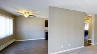 This single-floor residence offers a clean, functional layout designed for comfortable everyday living. The open floor plan seamlessly connects the living area to the kitchen, creating a sense of spaciousness and ease of movement throughout. Neutral warm-gray walls provide a versatile backdrop that complements a wide range of furnishing styles.

The living area features plush carpeting and is equipped with a ceiling fan with a built-in light fixture, ensuring year-round comfort. Transitioning toward the kitchen, the flooring shifts to durable hardwood-style planks, adding a practical and visually appealing contrast to the softer living space.

The kitchen is appointed with rich, dark cabinetry that creates a bold contrast against the lighter walls and countertops. A granite or stone-finish countertop adds a touch of refinement to the space. The layout is efficient, making the most of the available space for both cooking and storage.

Throughout the residence, clean white baseboards and trim offer a crisp finishing detail that ties the design together. The overall ambiance is modern and understated, with a neutral palette that feels bright and inviting. The thoughtful layout and quality finishes make this a well-appointed space suited for a variety of lifestyles.