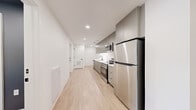 Located at 1704 North 17th Street in Tampa, FL, this single-story residence offers five bedrooms and six bathrooms across a thoughtfully designed floor plan. The interior reflects a clean, modern aesthetic defined by light wood flooring, crisp white walls, and consistent use of gray and neutral tones throughout.

The kitchen is efficiently laid out along a single wall and features stainless steel appliances — including a refrigerator, range, and microwave — complemented by gray cabinetry and recessed lighting overhead. The two living areas provide flexible common spaces; one is highlighted by a large black-framed window that frames a verdant outdoor view, allowing ample natural light to fill the room.

Each bedroom maintains the home's minimalist character, with select rooms showcasing accent walls in muted blue-gray tones and built-in cabinetry with integrated desks and wall-mounted media areas — ideal for both rest and productivity. The primary bedroom offers a notably generous footprint compared to the other rooms.

All six bathrooms are uniformly finished in light tile flooring, white walls, and matte black fixtures. Each includes a glass-enclosed shower, floating vanity with rectangular basin, and a large mirror — delivering a spa-like, contemporary feel. Six hallways connect the rooms efficiently, contributing to the home's well-organized and functional layout.