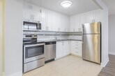 Located at 221 Queen St S in downtown Kitchener, this one-bedroom, one-bathroom unit offers a well-organized layout across a single floor. The open-concept design seamlessly connects the kitchen and living room, creating a bright and functional living space.

The kitchen is well-appointed with crisp white shaker-style cabinetry extending to the ceiling, dark granite countertops, a tiled backsplash, and a full suite of stainless steel appliances including a refrigerator, electric range, built-in microwave, and dishwasher. Light ceramic tile flooring completes the kitchen area.

The living room flows naturally from the kitchen and features warm wood-tone laminate flooring, neutral grey walls, and a stylish drum pendant light fixture. Large windows along the living area wall flood the space with natural light and offer views of the surrounding Kitchener cityscape, complemented by baseboard heating beneath the sills.

The bedroom is a comfortable size, featuring the same laminate flooring, a wide sliding mirrored closet, and a large window that continues the unit's theme of natural light and urban views.

The bathroom is finished with full-height beige wall tiles, a dark granite vanity countertop with an undermount sink, an oval pivot mirror, and chrome fixtures, giving it a clean and polished appearance.