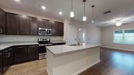 Located along Avalon Park East Boulevard in Orlando, Florida, this single-floor residence offers a thoughtfully designed layout with contemporary finishes throughout. The open-concept kitchen serves as a central highlight, showcasing rich dark cabinetry, speckled granite countertops, and a large central island with an integrated sink and pendant lighting overhead. Stainless steel appliances, including a refrigerator, range, and microwave, complete the well-appointed cooking space. Wood-style flooring flows through the kitchen and main living areas, adding warmth and continuity to the layout.

The living area is spacious and bright, benefiting from multiple windows that invite natural light and offer views of the surrounding neighborhood. Ceiling fans are present throughout, contributing to comfortable airflow. Bedrooms feature plush carpeting, generous windows with blinds, and walk-in closets equipped with wire shelving systems for organized storage.

The bathrooms mirror the kitchen's design aesthetic with dark vanity cabinetry, granite countertops, and wood-look flooring. One bathroom includes a tub-shower combination with clean white tile surround, while another features a glass-enclosed shower. Neutral wall tones and clean white trim maintain a cohesive, modern feel throughout the entire space.