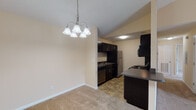 This single-floor residence features a thoughtfully designed layout that balances open common areas with defined private spaces. The living room stands out with its vaulted ceiling and ceiling fan, creating an airy, spacious atmosphere. A sliding glass door floods the area with natural light and provides outdoor access, while the front entry transitions from tile flooring to plush carpet throughout the main living areas.

The kitchen is designed in a galley style, featuring dark espresso cabinetry that contrasts sharply with granite-style dark countertops and stainless steel appliances, including a refrigerator, range, and microwave. Tile flooring runs through the kitchen and dining area, where a multi-light chandelier adds a decorative touch above the dining space. A peninsula counter connects the kitchen to the adjacent areas, enhancing the open-concept feel.

A hallway leads to the private quarters, including multiple bedrooms, each finished with soft carpet, neutral walls, and windows fitted with blinds. The primary bedroom features a tray ceiling detail and a ceiling fan. Bathrooms include tile flooring, a vanity with storage, and a full soaking tub and shower combination with clean, white surrounds—providing practical, everyday functionality throughout.