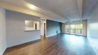 This single-floor unit combines a thoughtfully updated interior with a practical, open layout. The main living area is generously proportioned, featuring rich hardwood-style flooring, exposed structural beams overhead, and a textured ceiling that adds architectural character. A bold teal accent wall anchors the space, while a wall of sliding glass doors floods the room with natural light and provides direct access to a private balcony with outdoor views.

The galley-style kitchen is efficiently designed, offering grey cabinetry, quartz countertops, white subway tile backsplash, and black stainless appliances including a range, refrigerator, and dishwasher. A pass-through counter connects the kitchen to the main living space, enhancing the open feel.

The bedroom is a calm, well-proportioned room with beamed ceilings, hardwood-style flooring, and ample built-in closet storage. An en-suite bathroom features a quartz-topped vanity with a blue cabinet, elegant wall sconces, and open shelving for additional storage. The cohesive use of updated finishes and a neutral-to-cool color palette throughout gives the space a clean, modern character.