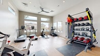 Located in Phoenix, AZ, this dedicated fitness center offers a comprehensive workout environment designed to support a wide range of exercise routines. The space features light hardwood-style flooring throughout, lofty ceilings, and an abundance of natural light streaming in through large floor-to-ceiling windows and transom windows positioned high on the walls, creating an open and energizing atmosphere. A ceiling fan provides additional air circulation, enhancing comfort during workouts.

The cardio zone is well-appointed with multiple treadmills, an elliptical trainer, a rowing machine, and a stationary spin bike, all positioned to take advantage of the views overlooking an outdoor pool and patio area. On the strength training side, the facility includes a multi-functional cable machine, an adjustable weight bench, a full rack of dumbbells, and a freestanding multi-tier rack stocked with kettlebells, medicine balls, slam balls, and resistance bands for functional fitness training. Protective floor mats are positioned throughout the space for safe equipment use.

Wall-mounted mirrors in the strength area enhance the sense of space and allow for proper form checks. The overall ambiance is clean, modern, and well-organized, making this fitness center a practical and inviting resource for daily exercise.