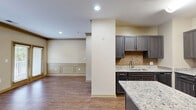 Located at 100 Maglaga Way in Locust Grove, Georgia, this one-bedroom, one-bathroom unit offers a well-designed single-floor layout that makes efficient use of its space. The open-concept kitchen and living area serves as the heart of the home, featuring rich hardwood-style flooring, crown molding, and a ceiling fan. The kitchen is well-appointed with dark wood cabinetry, granite-look countertops, a mosaic tile backsplash, a stainless steel dishwasher, an electric range, and a central island that provides additional workspace and storage. Large windows with blinds allow natural light to fill the living area, which also has direct access to a private balcony offering pleasant views of surrounding mature trees. The bedroom is comfortably sized, finished with plush carpeting, a ceiling fan, and windows that bring in natural light. It connects conveniently to a dedicated closet and hallway. The bathroom features a soaking tub and shower combination with decorative tile accents and wood-style flooring. A hallway connects all areas of the unit, maintaining a practical and cohesive flow throughout the home.