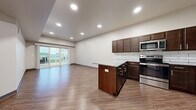 Located on S Homestead Dr in Andover, Kansas, this single-floor residence offers a thoughtfully designed layout with modern finishes and an efficient use of space. The open-concept kitchen and living area serves as the heart of the home, where rich dark-walnut cabinetry, stainless steel appliances, and granite countertops create a polished, functional kitchen. A subway tile backsplash adds a classic touch, while a central kitchen island provides additional prep and seating space. Wood-look plank flooring runs throughout, lending warmth and visual continuity across all rooms. The living area is bathed in natural light, thanks to a large sliding glass door that opens onto a private outdoor patio, offering views of the surrounding community. Recessed lighting complements the bright, neutral color palette throughout. The separate living room features a tray ceiling detail and a ceiling fan, adding architectural interest to the space. The bathroom mirrors the home's refined aesthetic with matching dark cabinetry, granite countertops, and a large vanity mirror. A dedicated walk-in closet provides wire shelving and ample storage. The overall ambiance is clean, contemporary, and move-in ready, ideal for those seeking comfortable, low-maintenance living in Andover.