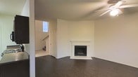 This two-story home offers a straightforward and functional layout designed to maximize livable space across both levels. The main living area makes an immediate impression with its rich, dark hardwood flooring that contrasts beautifully against the clean white walls, creating a bright and airy atmosphere throughout. A classically styled fireplace serves as the focal point of the living room, framed by a white mantel and raised hearth, adding both warmth and architectural character to the space. The ceiling fan overhead adds a practical touch to the room's comfort. Adjacent to the living area, a doorway leads to the entryway and staircase, where a window allows natural light to filter in, illuminating the transition between the lower and upper levels. The staircase connects seamlessly to the second floor, offering convenient access to the home's upper living spaces. The overall palette of the home is neutral and versatile, with white walls and trim throughout providing a clean canvas well-suited for a variety of interior styles. The combination of classic architectural details and practical design elements makes this a well-rounded two-story home.
