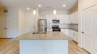 Located at 5895 Arbor Isle Way in Myrtle Beach, South Carolina, this single-floor residence offers a bright, open layout designed for comfortable living. The heart of the home is a well-appointed kitchen featuring crisp white shaker-style cabinetry, granite countertops, and a large central island with a built-in sink and pendant lighting overhead. Stainless steel appliances — including a refrigerator, range, and microwave — complement the subway tile backsplash, while light wood-style flooring ties the space together seamlessly. The kitchen opens directly into the living area, which is finished with plush carpeting, a ceiling fan, and glass sliding doors that lead to an outdoor deck, allowing natural light to pour into the space. A dedicated bedroom offers a relaxed, neutral palette with soft carpet underfoot and its own ceiling fan. The bathroom is finished with wood-look tile flooring, a granite-topped vanity with white cabinetry, and a full tub-shower combination with built-in shelving. Throughout the home, the clean white walls, recessed lighting, and consistent finishes create a cohesive and airy ambiance well-suited to the coastal Myrtle Beach lifestyle.