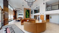 The Beekman Amenities level is designed to deliver a comprehensive lifestyle experience through a variety of thoughtfully curated spaces. The centerpiece is a grand lobby featuring soaring double-height ceilings, a dramatic cascading pendant light installation, and a striking circular channeled-leather sofa in warm cognac tones. A living green wall adds a natural focal point, while textured stone wall panels and large-format tile flooring contribute to the refined aesthetic. An adjacent community kitchen is outfitted with stainless steel appliances, dark cabinetry, white quartz countertops, and subway tile walls, opening toward a dining area ideal for gatherings. A fully equipped conference room offers a long wooden table, ergonomic seating, a textured accent wall, and access to an outdoor terrace. The fitness center provides an expansive array of cardio and strength equipment on patterned carpet tile flooring beneath bright, even lighting. Outdoor amenities include a resort-style pool surrounded by lounge chairs and a bold brick facade. A dedicated game room features a billiard table and built-in wood shelving, while a media lounge offers plush sectional seating and a large wall-mounted television, creating a relaxed retreat for residents.