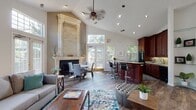Located at 3170 Mapleleaf Dr in Lexington, Kentucky, this single-floor space makes a striking first impression with its soaring vaulted ceilings and open-concept layout. The main living area is anchored by a dramatic floor-to-ceiling stone fireplace with an ornate carved surround, serving as a bold architectural centerpiece. A ceiling fan overhead and recessed lighting complement the airy feel of the space. Rich hardwood flooring flows continuously throughout, unifying the living, dining, and kitchen zones seamlessly.

The living area is generously proportioned, offering ample room for seating arrangements, and connects through an elegant arched opening to an adjacent room that functions as a private office or secondary lounge, complete with French doors and its own access to the outdoors. Large windows and glass-paned doors throughout the space invite an abundance of natural light and offer views of the surrounding greenery.

The kitchen is a standout feature, showcasing deep cherry wood cabinetry, light granite countertops with a complementary tile backsplash, and black appliances. A large wraparound island with bar seating provides additional workspace and a natural gathering point. Built-in glass corner shelving adds a refined display element. The dining area sits adjacent, bathed in natural light from nearby French doors leading outside.