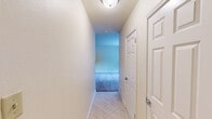 This single-floor unit offers a well-organized layout comprising a hallway, living room, kitchen, and bathroom, making efficient use of its compact footprint. The entryway hallway features light tile flooring and ceiling-mounted lighting, leading seamlessly into the main living areas.

The living room is a bright, open space with wall-to-wall carpeting in a neutral tone and soft beige walls that create a clean, welcoming atmosphere. A large window floods the room with natural light and offers a pleasant view of surrounding greenery. The room also includes a wall-mounted air conditioning unit and a closet, adding to its functionality.

The kitchen is thoughtfully appointed with warm oak cabinetry, light granite-style countertops, and a tile backsplash in a classic diagonal pattern. It is equipped with a full suite of appliances, including a refrigerator, electric range, and built-in microwave, along with a double-basin sink. Tile flooring ties the space together with a clean, practical finish.

The bathroom is accessible via the hallway and features tile flooring, a full soaking tub with a tiled surround accented by a decorative mosaic border, a vanity with dark wood cabinetry, and a toilet. The neutral color palette throughout the unit creates a cohesive and move-in ready environment.