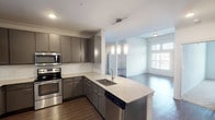 This single-floor residence is designed with a contemporary aesthetic and functional layout. The kitchen serves as a central highlight, showcasing grey shaker-style cabinetry with crown molding, granite countertops, and a classic white subway tile backsplash. A full suite of stainless steel appliances includes a French door refrigerator, electric range with over-the-range microwave, and dishwasher. A peninsula island with an undermount sink is illuminated by modern pendant lighting, and the space flows seamlessly into an open living area featuring wood-style hard flooring and a ceiling fan.

The bedrooms feature plush carpeting and notably tall ceilings that create an airy, open atmosphere. Each room benefits from generous natural light through large windows fitted with horizontal blinds, and each includes a closet with rod storage. One bedroom connects directly to a full bathroom, enhancing privacy.

The bathrooms are finished with granite-topped vanities featuring undermount sinks, dark cabinetry, and soaking tub and shower combinations tiled in crisp white subway tile with brushed nickel fixtures. Hard flooring in the bathrooms ties cohesively to the main living areas, giving the unit a polished, uniform finish throughout.