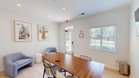 Located at 6001 Thomaston Rd in Macon, Georgia, this single-floor office space offers a clean, modern environment designed for focused work and collaborative meetings. The room is finished with bright white walls and light hardwood flooring, creating a fresh and professional atmosphere throughout.

At the center of the space sits a substantial walnut conference table surrounded by black wire-frame chairs, providing a functional hub for meetings and discussions. A wall-mounted flat-screen display and a frameless glass whiteboard offer versatile presentation and brainstorming tools, making the space well-equipped for professional use.

A cozy lounge corner features two soft blue upholstered chairs and a round accent table, offering an inviting area for informal conversations or a brief respite. The walls are accented with framed artwork depicting musical instruments, lending a creative and cultured character to the office environment.

Natural light filters in through a slatted-blind window and a glass-paneled exterior door, which provides direct outdoor views of the surrounding greenery and parking area. Recessed ceiling lighting supplements the natural light, ensuring a well-illuminated workspace at all times. The space connects to an adjacent area through an interior door, adding practical flow to the layout. Overall, this office strikes a balance between functionality and approachable design.
