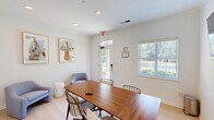 Located at 6001 Thomaston Rd in Macon, Georgia, this single-floor office space offers a clean, modern environment designed for focused work and collaborative meetings. The room is finished with bright white walls and light hardwood flooring, creating a fresh and professional atmosphere throughout.

At the center of the space sits a substantial walnut conference table surrounded by black wire-frame chairs, providing a functional hub for meetings and discussions. A wall-mounted flat-screen display and a frameless glass whiteboard offer versatile presentation and brainstorming tools, making the space well-equipped for professional use.

A cozy lounge corner features two soft blue upholstered chairs and a round accent table, offering an inviting area for informal conversations or a brief respite. The walls are accented with framed artwork depicting musical instruments, lending a creative and cultured character to the office environment.

Natural light filters in through a slatted-blind window and a glass-paneled exterior door, which provides direct outdoor views of the surrounding greenery and parking area. Recessed ceiling lighting supplements the natural light, ensuring a well-illuminated workspace at all times. The space connects to an adjacent area through an interior door, adding practical flow to the layout. Overall, this office strikes a balance between functionality and approachable design.