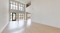 Located in San Antonio, TX, this contemporary two-story residence offers a thoughtfully designed layout across two floors. The main level is immediately striking, featuring soaring double-height ceilings and an expansive wall of black-framed, floor-to-ceiling windows that flood the open living area with abundant natural light and offer views of the surrounding greenery. Light-toned wood flooring runs seamlessly throughout, enhancing the bright, airy ambiance.

The modern kitchen is well-appointed with natural wood-finish cabinetry extending to the ceiling, stainless steel appliances including a French door refrigerator, built-in microwave, and range, along with a clean white countertop island. A utility room and a patio with a classic brick surround and open outdoor views complete the ground floor.

The upper level houses the generously sized primary bedroom, which features a ceiling fan, large French doors with blinds for natural light control, and access to two well-organized closets with built-in shelving and hanging rails. Two full bathrooms serve the residence, one of which is equipped with accessibility grab bars. Two staircases connect the floors, adding functional flow to the layout.