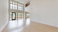 Located in San Antonio, TX, this contemporary two-story residence offers a thoughtfully designed layout across two floors. The main level is immediately striking, featuring soaring double-height ceilings and an expansive wall of black-framed, floor-to-ceiling windows that flood the open living area with abundant natural light and offer views of the surrounding greenery. Light-toned wood flooring runs seamlessly throughout, enhancing the bright, airy ambiance.

The modern kitchen is well-appointed with natural wood-finish cabinetry extending to the ceiling, stainless steel appliances including a French door refrigerator, built-in microwave, and range, along with a clean white countertop island. A utility room and a patio with a classic brick surround and open outdoor views complete the ground floor.

The upper level houses the generously sized primary bedroom, which features a ceiling fan, large French doors with blinds for natural light control, and access to two well-organized closets with built-in shelving and hanging rails. Two full bathrooms serve the residence, one of which is equipped with accessibility grab bars. Two staircases connect the floors, adding functional flow to the layout.