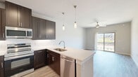 This thoughtfully designed one-bedroom, one-bathroom unit in Corinth, Texas offers a functional and modern living experience across a single floor. The open-concept layout seamlessly connects the kitchen, dining area, and living room, creating a bright and cohesive space. The kitchen is a standout feature, showcasing rich dark espresso cabinetry, a white quartz peninsula with an undermount sink, a classic white tile backsplash, and a full suite of stainless steel appliances including a refrigerator, range, microwave, and dishwasher. Stylish pendant lighting over the peninsula adds a refined touch. Light wood-look flooring runs throughout the main living areas, complementing the neutral, warm-toned walls. The living area is bathed in natural light and opens directly to a private patio through sliding glass doors, offering outdoor views. The carpeted bedroom is a comfortable retreat, fitted with a ceiling fan and a window with outdoor views. Two closets provide ample storage. The bathroom features a dark wood vanity with quartz countertops, a large mirror, overhead cabinetry, and a tub-shower combination. A hallway connects all areas efficiently, making this unit practical and well-organized throughout.