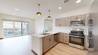 Located at 1990 Rimel Rd in Missoula, Montana, this modern unit offers five bedrooms and two bathrooms across a single floor. The open-concept kitchen is a standout feature, equipped with stainless steel appliances including a gas range, microwave, dishwasher, and refrigerator. Light wood-grain cabinetry, white quartz countertops, a peninsula with a sink, and a white subway tile backsplash give the kitchen a clean, contemporary aesthetic. Stylish black dome pendant lights add a modern touch overhead. Light hardwood-style flooring flows throughout the common areas, leading to a bright living space with sliding glass doors that open to a private balcony overlooking scenic Missoula hillsides. The bedrooms feature plush carpeting, ceiling fans, and large windows that invite natural light and outdoor views. Closets throughout provide ample storage, including walk-in and double-door configurations. The bathrooms are finished with wood-grain vanities, white quartz countertops, and light hardwood-style flooring; one includes a full soaking tub and shower combo, while the other features a sleek walk-in shower area. The overall design is clean, bright, and well-appointed, reflecting a contemporary Missoula lifestyle.