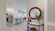 This single-floor residence offers a thoughtfully designed open-concept layout that seamlessly connects the kitchen, dining, and living areas. The entryway sets an inviting tone, featuring a decorative console table and a distinctive circular mirror. Light wood-style flooring flows throughout the main living spaces, complementing the bright, neutral color palette.

The kitchen is well-equipped with gray shaker-style cabinetry, granite countertops, stainless steel appliances, and a peninsula island with bar seating. Pendant lighting above the island adds a polished finishing touch. The adjoining living room benefits from natural light through large windows and offers a comfortable, stylish atmosphere.

The primary bedroom features elevated ceilings, plush carpet, and an en-suite bathroom complete with a granite-topped dual vanity, wood-look tile flooring, and a glass-enclosed walk-in shower. A second bedroom, also carpeted, includes generous window placement for natural light. A secondary bathroom provides a tiled tub-shower combination with a coordinating vanity. Additional bedrooms are bright and comfortably scaled, each with neutral finishes and window treatments that allow for natural light control.