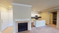 Located at 3601 Grapevine Mills Pkwy Frontage Rd in Grapevine, TX, this single-floor residence offers a well-designed open-concept layout that seamlessly connects the living and kitchen areas. The living space is anchored by a classic tile-surround fireplace with a white-painted mantel and crown molding detail, adding a refined architectural touch to the room. Warm neutral tones and plush carpeting throughout the living and bedroom areas create a comfortable, cohesive atmosphere.

The kitchen is a functional centerpiece of the home, featuring crisp white cabinetry, a dark tile backsplash, and a peninsula island topped with light granite countertops and an undermount double sink. Stainless steel appliances — including a refrigerator, range, and over-the-range microwave — complete the kitchen. Recessed lighting and crown molding carry through this space as well. Wood-look flooring in the kitchen adds contrast and durability.

The bedrooms are carpeted and receive natural light through slatted windows, with ceiling fans providing additional comfort. A built-in shelving nook is visible off the main living area, offering practical storage. The bathroom includes a full tub-shower combination with white tile surround and wood-look flooring. Overall, the space presents a clean, move-in-ready interior with consistent finishes throughout.