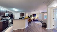 Located at 212 Katherine Blvd in Palm Harbor, Florida, this single-floor residence offers a well-designed open-concept layout that seamlessly connects the kitchen, dining, and living areas. The kitchen is equipped with dark espresso cabinetry, granite countertops, black appliances including a range, microwave, refrigerator, and dishwasher, and a peninsula island with bar seating — ideal for casual dining and entertaining. Crown molding and wood-look flooring extend throughout the main living areas, adding a polished, cohesive feel. The living room is generously proportioned, featuring a ceiling fan, an electric fireplace, and sliding glass doors that open to an outdoor balcony, allowing ample natural light to fill the space. A dedicated dining area accommodates a glass-top table and tufted seating beneath a pendant light. The bedrooms offer plush carpeting, ceiling fans, and large windows that invite natural light. The primary bedroom includes an en-suite bath. The bathrooms feature granite vanity countertops, dark cabinetry, and wood-look flooring. Throughout, the home presents a warm, neutral palette complemented by tasteful finishes, making it a comfortable and move-in-ready residence in Palm Harbor.