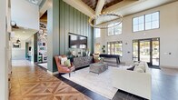 Located at 4820 SW 48th Ave in Ocala, Florida, this single-floor community clubhouse offers a generously proportioned, open-plan interior defined by dramatic double-height ceilings and an abundance of natural light streaming through oversized windows and glass doors. The space features a sophisticated blend of materials, including intricate herringbone and parquet-patterned hardwood flooring alongside dark polished tile, creating a visually dynamic foundation throughout.

The main lounge area is anchored by a bold green shiplap accent wall with a mounted flat-screen television, complemented by a curated arrangement of leather wingback chairs, a sectional sofa, and a metal-framed coffee table beneath a striking circular chandelier. Adjacent to the lounge, a full billiards zone showcases a professional-grade pool table set against a floor-to-ceiling gallery wall densely covered in eclectic framed artwork, adding a creative and vibrant focal point.

A bar and social area features a dark countertop island lined with elegant white upholstered bar stools, positioned beneath decorative green tile detailing and additional display shelving. Exposed wooden ceiling beams with cross-bracing lend a warm, architectural character to the space. A cozy windowed banquette nook with leather seating and pendant lighting provides an intimate setting for smaller gatherings. Large glazed doors open to outdoor views, reinforcing the bright and welcoming ambiance of this well-appointed communal facility.
