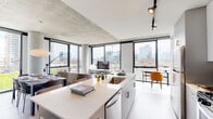 Located in Chicago's vibrant West Loop neighborhood, this contemporary residence at 160 N Elizabeth Street showcases a refined industrial-modern aesthetic. The open-concept living and dining area is anchored by expansive floor-to-ceiling windows on multiple walls, flooding the space with natural light and offering striking panoramic views of the Chicago skyline and surrounding cityscape. Exposed concrete ceilings and structural columns lend an architectural authenticity throughout.

The kitchen is equipped with stainless steel appliances, sleek gray cabinetry, a gas range, and a large white quartz island with bar seating — ideal for both cooking and casual dining. Track lighting and bold accent walls add character and depth.

The living area is defined by its corner window configuration, where a cylindrical concrete column frames sweeping city views, creating a dramatic yet intimate setting. The bedrooms continue the floor-to-ceiling window theme, with one featuring direct access to a private outdoor balcony and exposed concrete accent walls, while city views serve as a natural backdrop.

The bathroom is clean and well-appointed, featuring subway tile surround, a soaking tub, a gray vanity, and an illuminated mirror. Dark hardwood flooring flows throughout, complemented by crisp white walls and a hallway with textured concrete ceiling details.