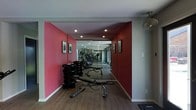 This single-floor fitness space is thoughtfully designed to support a comprehensive workout experience. The room features striking red accent walls that energize the environment, contrasting cleanly with light grey upper walls and a white ceiling. Warm hardwood-style flooring runs throughout, adding a polished, durable surface underfoot.

Recessed ceiling lights provide consistent, even illumination across the space, while a ceiling fan mounted near the entry ensures proper air circulation during intense workouts. A full-length mirrored wall at the far end visually expands the room, creating a sense of greater depth while also serving as a practical training aid for monitoring form.

The space is well-stocked with strength and cardio equipment, including a multi-position adjustable weight bench, a rack of dumbbells, and cardio machines such as ellipticals and treadmills arranged toward the rear. Framed artwork on the walls adds a refined touch, elevating the space beyond a purely utilitarian gym. Overall, the layout is organized and functional, offering an efficient flow between equipment zones within a motivating, well-appointed environment.