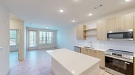 This thoughtfully designed one-bedroom, one-bathroom residence in Charlotte, NC offers a clean, modern aesthetic throughout. Light wood-style flooring flows seamlessly across the entire space, creating a bright and cohesive atmosphere. The open-concept kitchen and living area serves as the heart of the unit, featuring light wood cabinetry, white quartz countertops, a central island, and a full suite of stainless steel appliances including a refrigerator, range, microwave, and dishwasher. Recessed lighting illuminates the kitchen, complemented by ample cabinet storage. The living area is well-lit by a large window and a glass-paneled door that opens to a private balcony, offering views of the surrounding community. The bedroom is a comfortable retreat equipped with a ceiling fan, a large window with natural light, and direct access to the bathroom. The bathroom features a wide vanity with wood-toned cabinetry, white countertops, and a large mirror. A dedicated closet and in-unit washer and dryer hookups add functional convenience. The overall ambiance is contemporary and bright, with a neutral color palette that enhances the sense of openness throughout.