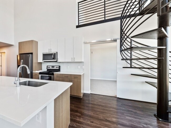 2 Bedroom w/ Loft with spiral staircase and two-tone walnut cabinetry and pearl countertops. - 24Fifty at University Park