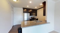 Located at 3381 Blue Heron Dr in Hilliard, Ohio, this single-floor residence offers a thoughtfully designed layout with modern finishes throughout. The kitchen serves as a standout feature, showcasing rich, dark espresso cabinetry that extends to the ceiling for ample storage. Stainless steel appliances — including a refrigerator, gas range, and built-in microwave — complement the sleek aesthetic. A peninsula with granite-style countertops provides additional workspace and casual seating, making the kitchen ideal for both cooking and entertaining. Recessed lighting illuminates the space with a clean, modern glow, while dark hardwood-style flooring adds warmth and continuity throughout the open area. The entry door is conveniently accessible directly from the kitchen and living space, contributing to a practical and efficient floor plan. Overall, the space balances functionality with contemporary style, featuring a neutral color palette that creates a bright and welcoming ambiance suited for everyday living.