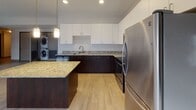 Located at 234–298 N St Clair St in downtown Toledo, Ohio, this single-floor unit offers a well-organized layout that balances open communal areas with private living spaces. The kitchen serves as a central highlight, featuring dark espresso cabinetry paired with white upper cabinets and granite countertops throughout, including on a functional center island. Stainless steel appliances, recessed and pendant lighting, and light wood-style flooring complete the contemporary aesthetic. In-unit stacked washer and dryer are conveniently integrated into the kitchen area.

The open living area adjoins the kitchen seamlessly, with the same light flooring extending throughout for a cohesive look. Bedrooms are carpeted for comfort, offering neutral tones, baseboard heating, closet storage, and access to natural light through windows fitted with roller shades. Dark-trimmed door frames provide a consistent design detail across the unit.

The bathroom is finished with a dark espresso vanity, a light countertop, a large mirror with overhead lighting, and a full tub and shower combination with chrome fixtures. The overall design is clean and modern, with a neutral color palette and consistent finishes creating a cohesive, move-in-ready environment.
