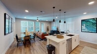 Located at 1701 Central Ave in St. Petersburg, Florida, this well-appointed single-floor residence offers a thoughtfully designed open-concept layout. The kitchen is a standout feature, showcasing white cabinetry, quartz countertops, stainless steel appliances, and a large center island with seating — illuminated by a trio of sleek pendant lights. The kitchen flows seamlessly into the living and dining areas, where light wood-style flooring, recessed lighting, and ceiling fans create a bright, comfortable atmosphere. Large windows throughout the main living space invite abundant natural light. The dining area accommodates a full-sized table and is accented by bold wall art, while a secondary flex room offers space for a home office or sitting room with plush carpeting and a ceiling fan. The bedrooms are carpeted and generously sized, each equipped with ceiling fans and walk-in closets. The primary suite connects to a well-designed en-suite bathroom featuring wood-look flooring, a glass-enclosed shower, a floating vanity with quartz countertops, and direct access to a spacious walk-in closet. A second full bathroom mirrors the same clean, modern aesthetic with bright white finishes and updated fixtures.