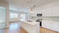 This well-appointed single-floor residence offers a clean, modern aesthetic defined by crisp white walls, light hardwood-style flooring, and abundant natural light. The open-concept living area seamlessly connects the dining room, kitchen, and living room, creating a spacious and functional common area. The kitchen is a standout feature, boasting an expansive white quartz island with an integrated sink and a professional-style faucet, white shaker cabinetry with gold hardware, a light green subway tile backsplash, and a full suite of stainless steel appliances including a French door refrigerator, range, microwave, and dishwasher. Elegant brass pendant lights hang above the island, adding warmth to the bright space. Large windows frame outdoor views and bathe the living area in natural light. The two bedrooms are carpeted and offer ceiling fans, with the primary bedroom featuring access to a sleek en-suite bathroom appointed with a dual-sink vanity, illuminated mirrors, gold hardware, large-format tile flooring, and a glass-enclosed shower. A dedicated laundry room houses a stacked full-size washer and dryer. Four well-organized closets provide exceptional storage, complemented by a convenient hallway connecting all areas of the home.
