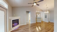 This well-designed single-floor residence in Biloxi, Mississippi, showcases a thoughtful open-concept layout with a bright, contemporary aesthetic throughout. The main living area immediately draws attention with its vaulted ceilings and a modern electric fireplace set into a clean white surround, creating a striking focal point. A ceiling fan overhead and natural light from front-facing windows enhance the airy atmosphere, while warm-toned hardwood-style flooring extends throughout the main living spaces.

The kitchen is both functional and stylish, featuring white shaker cabinetry, light quartz countertops, a subway tile backsplash, and a full suite of stainless steel appliances including a refrigerator, range, and over-the-range microwave. A peninsula with pendant lighting connects the kitchen to the living and dining area, adding an elegant transitional element complemented by a chandelier above.

The bedrooms are carpeted for comfort, each with ceiling fans and natural light from windows with blinds. One bedroom includes two closets, providing ample storage. The bathroom is neatly appointed with a tiled tub-shower combination, white vanity cabinetry, and brushed nickel fixtures, maintaining the space's clean, modern character throughout.