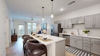 This well-appointed single-floor residence showcases a thoughtfully designed open-concept layout that seamlessly connects the kitchen, dining, and living areas. The kitchen is a standout feature, equipped with stainless steel appliances, grey shaker-style cabinetry, white quartz countertops, and a classic subway tile backsplash. A generously sized kitchen island with seating for multiple guests serves as the centerpiece, illuminated by stylish pendant lighting overhead. Light wood-style flooring runs throughout the main living areas, enhancing the bright, airy atmosphere created by abundant natural light from large windows.

The living area offers a comfortable and inviting retreat, featuring neutral tones and access to natural light through sizable windows with outdoor views. Two well-sized bedrooms are carpeted for comfort, each featuring ceiling fans, large windows with outdoor views, and ample natural light. The primary bedroom includes a walk-in closet outfitted with wire shelving and storage solutions. The primary bathroom is finished with grey cabinetry, white quartz countertops, a dual-sink vanity, wood-look flooring, and a glass-enclosed tiled shower. The overall aesthetic is clean, contemporary, and cohesive throughout.