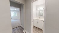 This well-appointed two-floor residence showcases a thoughtfully updated interior with a cohesive, modern aesthetic throughout. The main living area on the lower level is bright and open, featuring light-toned luxury vinyl plank flooring and recessed lighting. Large sliding glass doors connect the living space to an outdoor patio area, allowing natural light to fill the room. The kitchen is outfitted with crisp white shaker-style cabinetry, quartz countertops, a stainless steel undermount sink, and a stainless steel dishwasher, combining style with functionality. The bathroom features a clean, all-white design with a white vanity, quartz countertop, brushed nickel fixtures, a large framed mirror with overhead lighting, and wood-look flooring that ties seamlessly into the rest of the home. Bedrooms are finished with soft, neutral carpeting and windows that invite natural light, creating comfortable and serene retreats. The upper level is accessed via a staircase with a black metal railing, landing on an open landing area with wood-look flooring and recessed lighting. Throughout the home, neutral gray walls, white trim, and consistent finishes create a cohesive, move-in-ready environment.