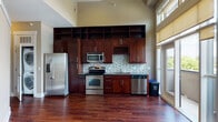 Located at 600 St. Mary's St in Raleigh, NC, this single-floor unit showcases a thoughtfully designed interior with an open, airy feel defined by soaring ceilings and rich hardwood flooring throughout the main living areas. The kitchen is a standout feature, outfitted with full-height dark cherry cabinetry, a mosaic tile backsplash, stainless steel appliances including a refrigerator, range, microwave, and dishwasher, and sleek countertops. A dedicated wine rack built into the upper cabinetry adds a refined touch. Floor-to-ceiling windows and a sliding glass door flood the living space with natural light and provide direct access to a private balcony overlooking the surrounding cityscape. The bedroom features hardwood floors, a ceiling fan, and additional windows that frame outdoor views, while a secondary room is finished with neutral carpet and an elegant tray ceiling detail. The bathroom is appointed with full tile surround, a soaking tub, and a classic mosaic accent border. The open layout and elevated ceiling heights create a generous sense of space throughout, making this a well-appointed urban residence in the heart of Raleigh.