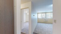 This 1-bedroom, 1-bathroom apartment in Richfield, Minnesota offers a practical and well-organized layout across a single floor. The living and kitchen area features durable wood-look flooring, white cabinetry with open shelving, a stainless steel dishwasher, a full-size refrigerator, and a sink with countertop workspace. Track lighting overhead keeps the kitchen bright and functional. A hallway connects the main living area to the bedroom, providing a natural separation between spaces. The bedroom is comfortably sized, finished with neutral carpet, and equipped with a ceiling fan with integrated lighting. A large window dressed with vertical blinds allows natural light to filter in while offering views of the surrounding greenery. A wall-mounted air conditioning unit and baseboard heating ensure year-round comfort. A full-width louvered bi-fold closet provides generous storage. The living area, also carpeted, benefits from additional windows with vertical blinds that bring in natural light and outdoor views. The overall aesthetic is clean and neutral, with white walls and simple finishes that create a bright, move-in-ready atmosphere throughout.
