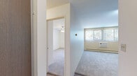 This 1-bedroom, 1-bathroom apartment in Richfield, Minnesota offers a practical and well-organized layout across a single floor. The living and kitchen area features durable wood-look flooring, white cabinetry with open shelving, a stainless steel dishwasher, a full-size refrigerator, and a sink with countertop workspace. Track lighting overhead keeps the kitchen bright and functional. A hallway connects the main living area to the bedroom, providing a natural separation between spaces. The bedroom is comfortably sized, finished with neutral carpet, and equipped with a ceiling fan with integrated lighting. A large window dressed with vertical blinds allows natural light to filter in while offering views of the surrounding greenery. A wall-mounted air conditioning unit and baseboard heating ensure year-round comfort. A full-width louvered bi-fold closet provides generous storage. The living area, also carpeted, benefits from additional windows with vertical blinds that bring in natural light and outdoor views. The overall aesthetic is clean and neutral, with white walls and simple finishes that create a bright, move-in-ready atmosphere throughout.