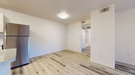 This single-floor unit offers a clean, modern aesthetic defined by light wood-style flooring that extends seamlessly throughout every room, creating a cohesive and airy feel. The open kitchen is well-appointed with crisp white cabinetry, stone-look countertops, a stainless steel refrigerator, dishwasher, and range, along with a double-basin sink positioned beneath a window with vertical blinds that allow in natural light. A peninsula counter provides additional workspace and enhances the open flow between the kitchen and living areas. The living space features a ceiling fan and sliding glass doors that open to an outdoor area, filling the room with abundant natural light and views of the surroundings. Multiple generously sized rooms offer flexibility, each featuring the same durable light wood-style flooring and bright white walls that lend a fresh, neutral palette. The bathroom is finished with a single-sink vanity topped with a speckled countertop and a large mirror, complemented by matching light flooring. A dedicated laundry closet houses a top-loading washer and overhead shelving, adding practical convenience. Throughout the unit, ceiling-mounted light fixtures, HVAC vents, and clean wall finishes underscore the move-in-ready condition of this well-designed space.